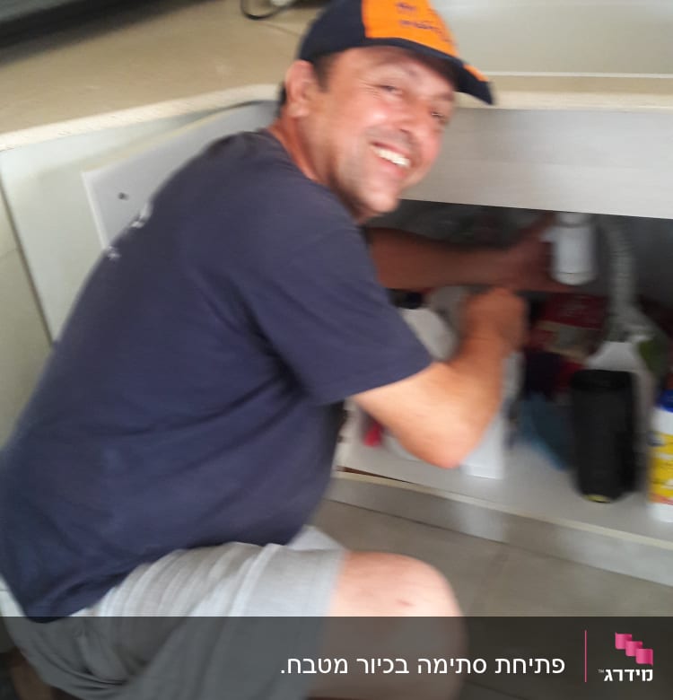 אדם מתקן צנרת מתחת לכיור במטבח
